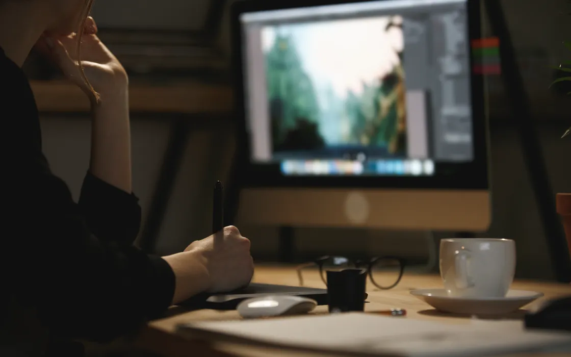 Gestalterin arbeitet mit Stift am Grafiktablett, vor ihr ein Bildschirm mit geöffnetem Bildbearbeitungsprogramm